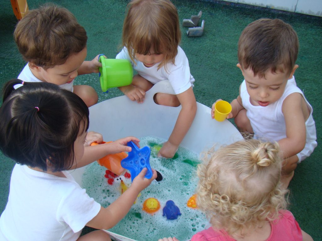 5 crianças em volta de uma pequena piscina brincando juntas.