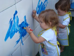 Duas crianças pintando a parede do ateliêr de artes com tinta azul