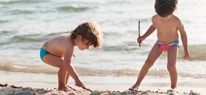 Duas crianças brincando na areia, mar no fundo da imagem.